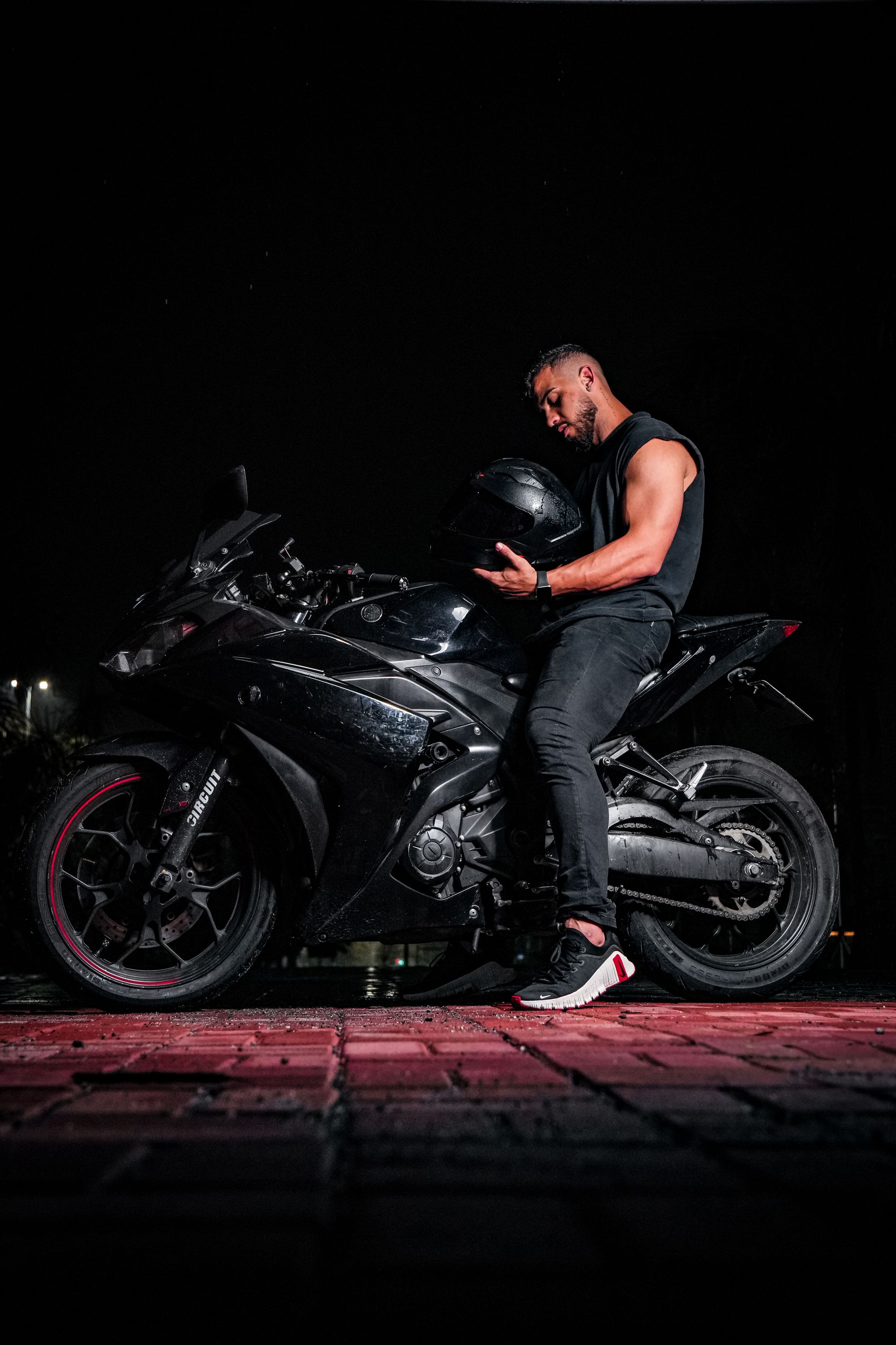 Rider sitting on a black sportbike at night, holding a helmet